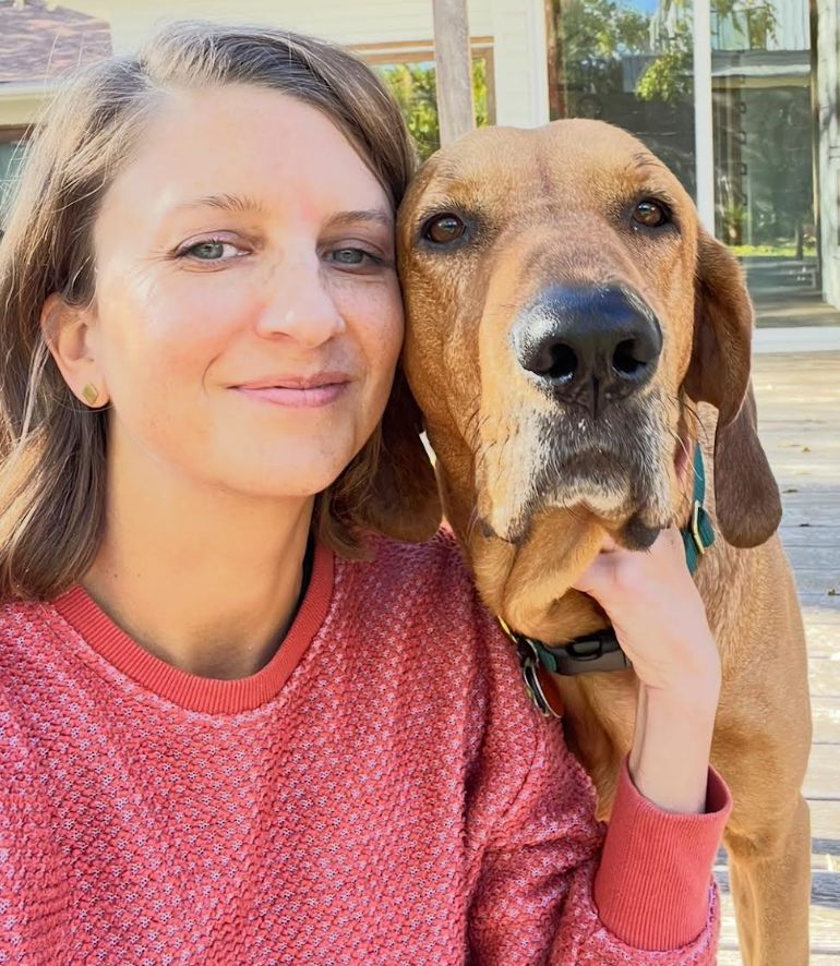 Amber Schleuning wears a red sweatshirt and poses with her dog